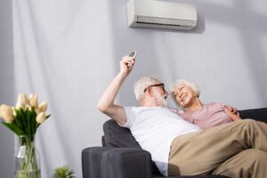 A homeowner checks a heat pump outdoor unit beside a house while warm air circulates indoors.